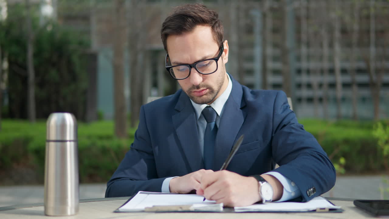 giovane uomo d'affari barbuto pensando e scrivendo appunti o evidenziando in un parco verde