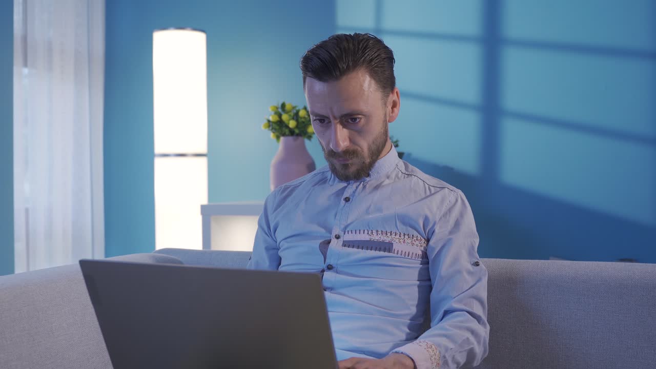 hombre elegante y elegante usando la computadora portátil por la noche de una manera seria y centrada en casa.