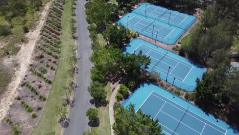 4k aerial view of four tennis courts next to a road in australia