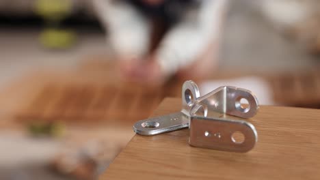 a metal bracket on a wooden surface with blurred background of furniture assembly, highlighting focus and depth of field