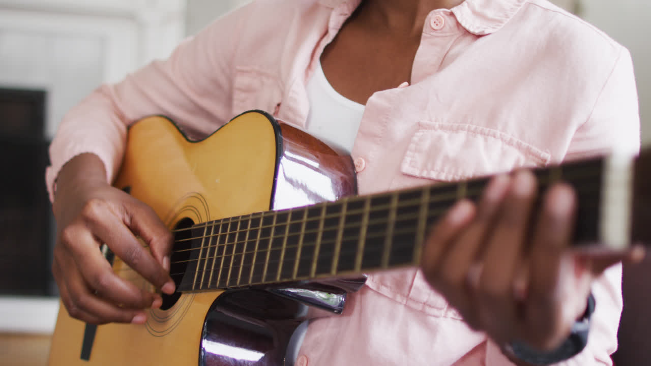 sección media de una mujer afroamericana tocando la guitarra en casa