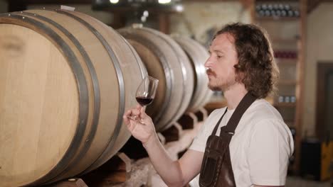 authentic shot of successful male sommelier is tasting a flavor and checking white wine quality poured in transparent glass in a wine cellar.