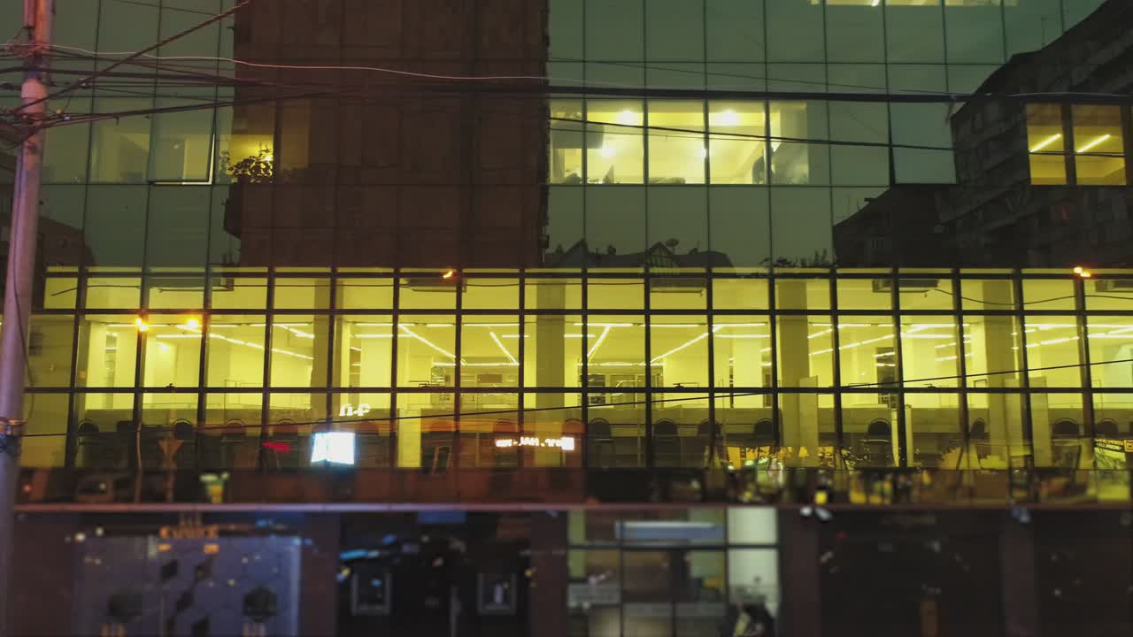 비즈니스 디스트릭트 건물의 4k 외관, 저녁이나 밤에 벽 거울 창문이있는 쇼핑몰, 거울 벽에 도시, 사람, 자동차의 반사, 드론 카메라 이동, 내부에서 일하는 사람들