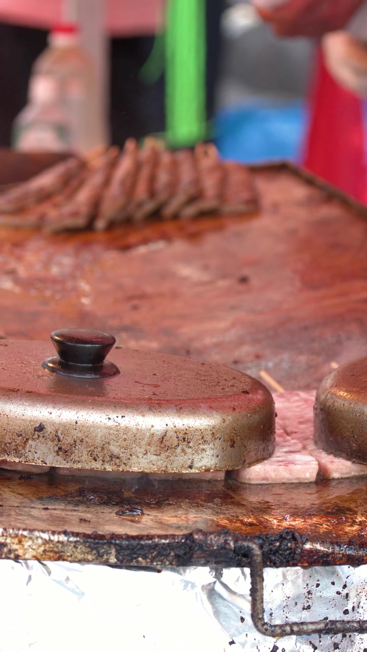 Primo piano di spiedini di carne che cuociono sotto coperchi di metallo su una piastra teppanyaki rovente all'aperto
