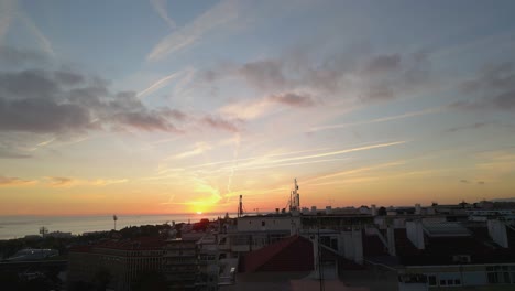 Aerial-view-of-a-sunset-in-Lisbon-Bay,-nestled-in-the-midst-of-houses-near-the-Tagus-River,-painting-the-sky-and-water-with-warm-hues-amid-the-urban-landscape