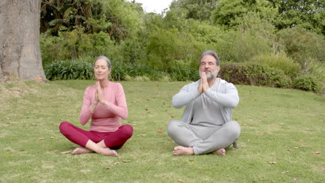 mature couple meditating outdoors, sitting cross-legged on grass, finding peace