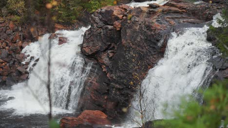 Concealed-within-the-autumn-forest,-a-waterfall-cascades-over-dark-rocks,-its-serene-beauty-adding-enchantment-to-the-secluded-woodland-scenery