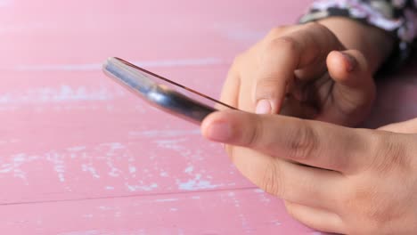 persona usando un teléfono inteligente en una mesa rosa