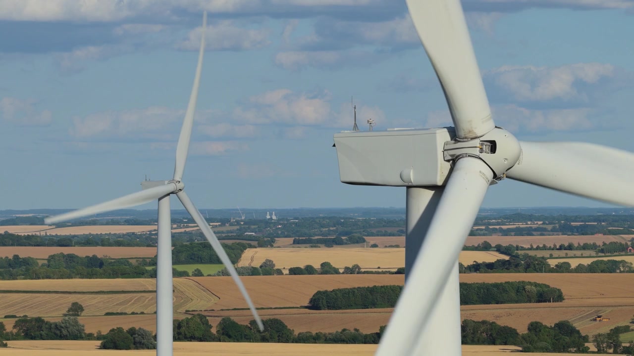 Aerogeneradores blancos giran para generar electricidad limpia y renovable sobre extensos campos agrícolas rurales en un día brillante y despejado en el campo de Europa durante el verano