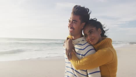 retrato de una pareja hispana sonriente de pie y abrazándose en la playa