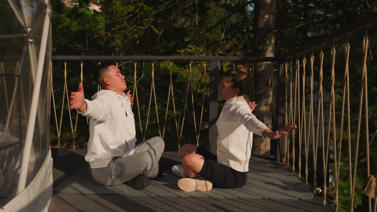 compañeros hacen yoga extendiendo los brazos en glamping. hermano y hermana respiran profundamente aire fresco meditando en la terraza del hotel ecológico. recreación del cuerpo y la mente