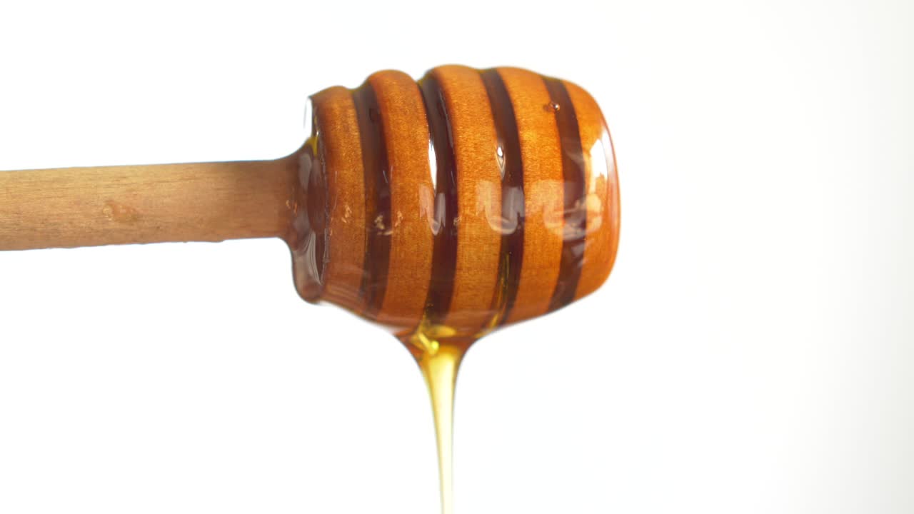 Fresh honey pouring from a wooden spoon