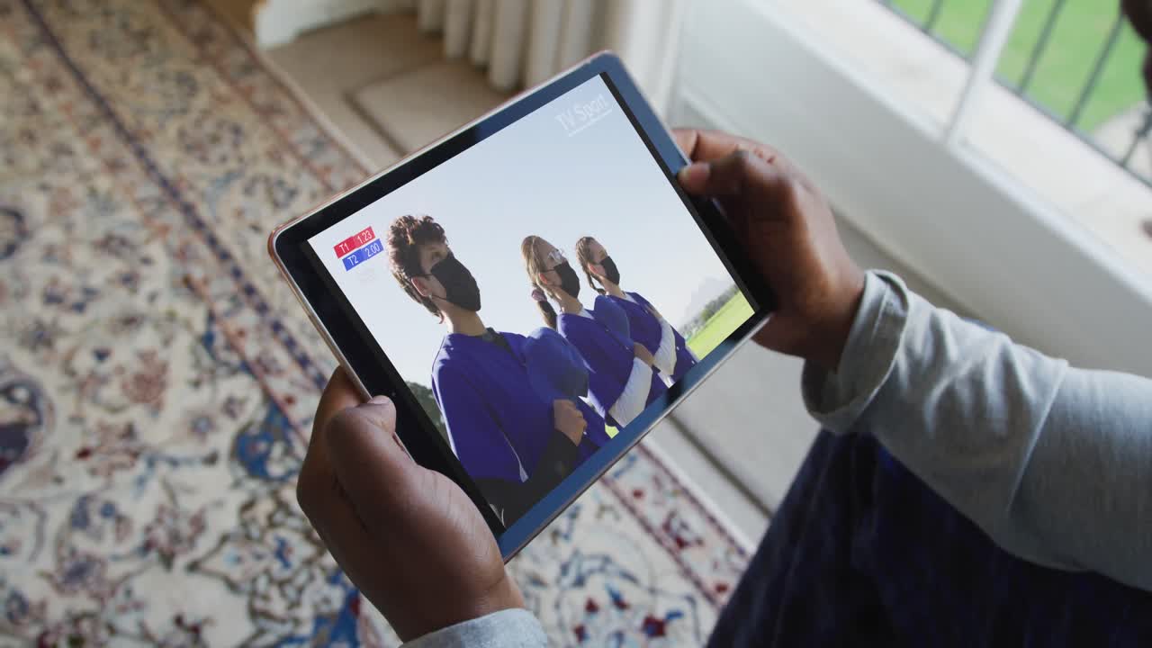 compuesto de un hombre sentado en casa, viendo un juego de béisbol durante la covid 19 en una tableta