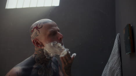 tattooed inmate applying shaving foam to his face during morning in prison