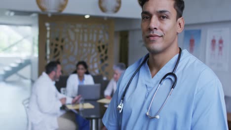 Portrait-of-mixed-race-male-doctor-smiling,-with-colleagues-in-discussion-in-background