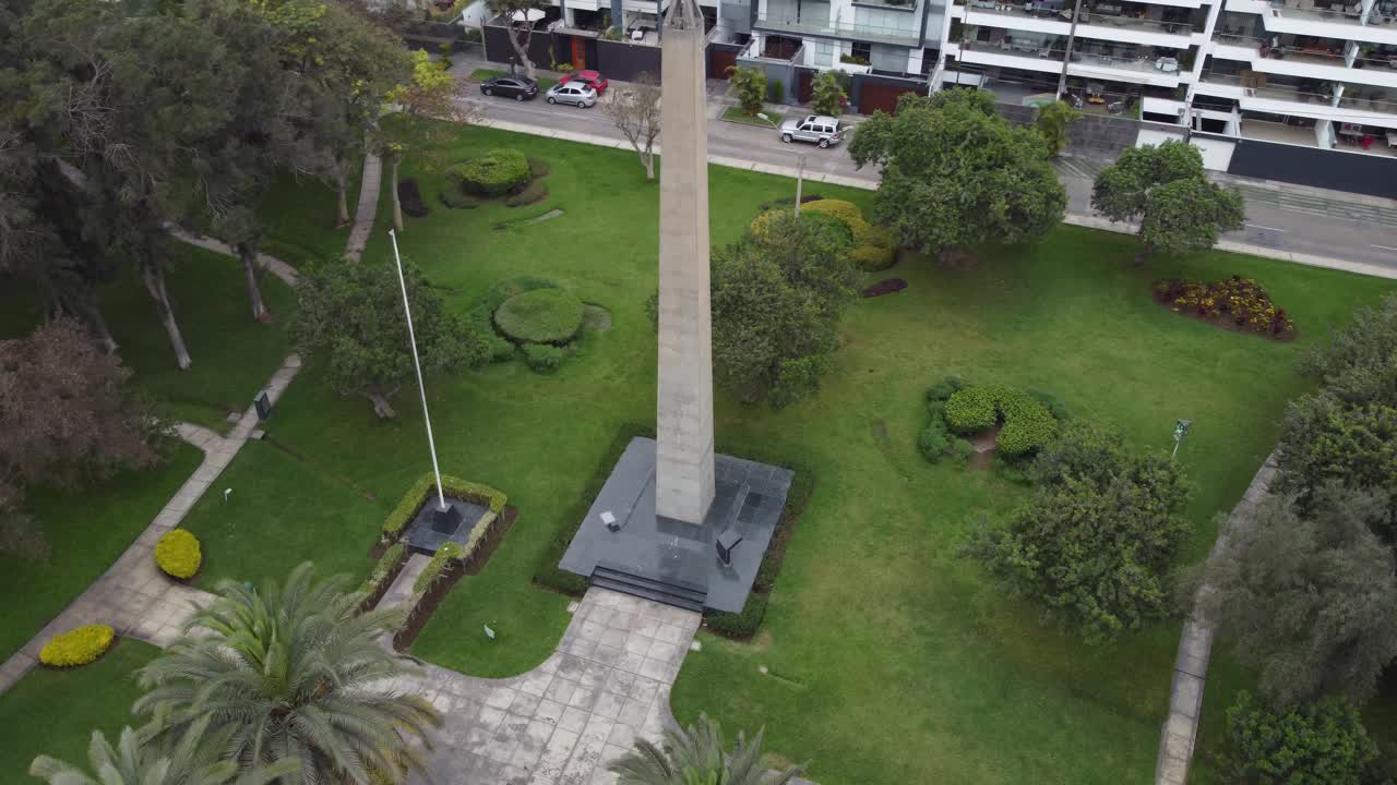 video de drones de 4k de un obelisco en un parque, rodeado de árboles y hierba verde y un asta de bandera