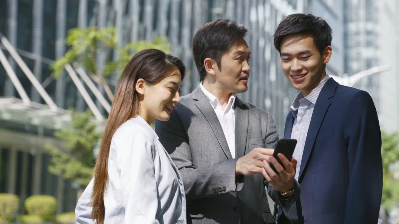 asian businesspeople standing on street looking at mobile phone in modern city