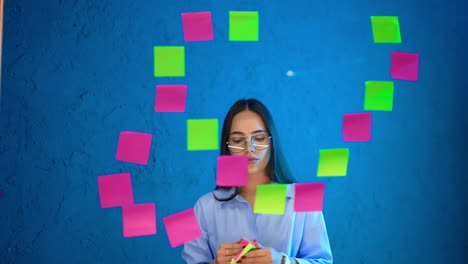 woman notes in office. a woman in glasses uses sticky notes to organize ideas on a blue wall in a modern office setting during the day