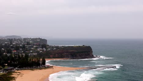 Overcast-day-at-a-coastal-cliffside-and-beach-community,-Waves-washing-ashore-on-a-sandy-beach