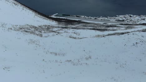 Drone-view-in-Tromso-area-in-winter-flying-over-a-snowy-mountain-and-looking-down-into-the-fjord-in-Segla,-Norway