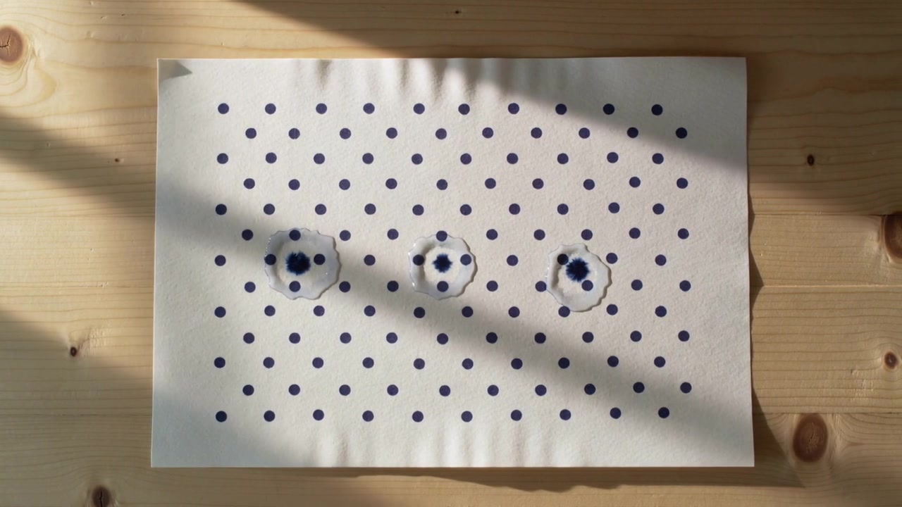 Registrazione di un lenzuolo a pois blu navy con tre segni centrali che si approfondiscono su un tavolo di legno con il sole che si sposta.