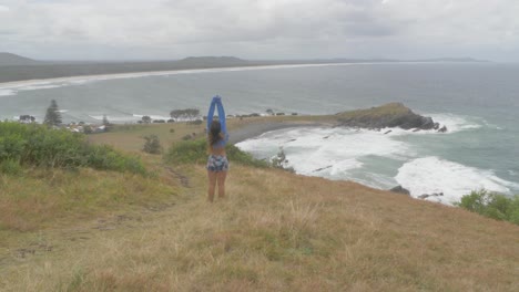 sexy caucasian woman standing and raising hands in the air on a windy morning - crescent head lookout at crescent head of sydney in kempsey shire, new south wales, australia