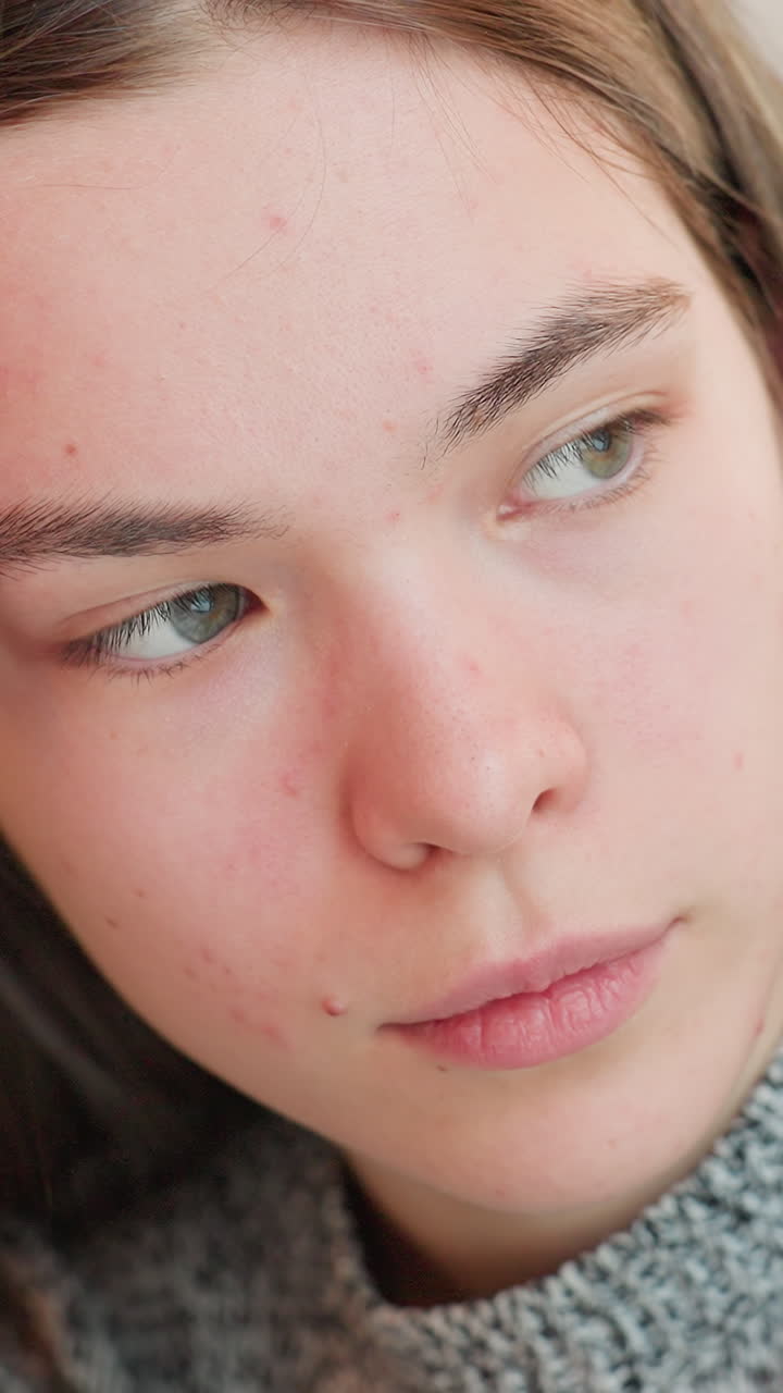 Primo piano di una giovane donna esposta a una luce naturale soffusa, texture della pelle delicata e incarnato reale visibili mentre gli occhi si muovono in tranquilla contemplazione; l'inquadratura suggerisce i ruoli di studentessa, modella e amica intima.
