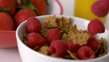 Raspberries-pouring-into-cereal-bowl-at-breakfast-table