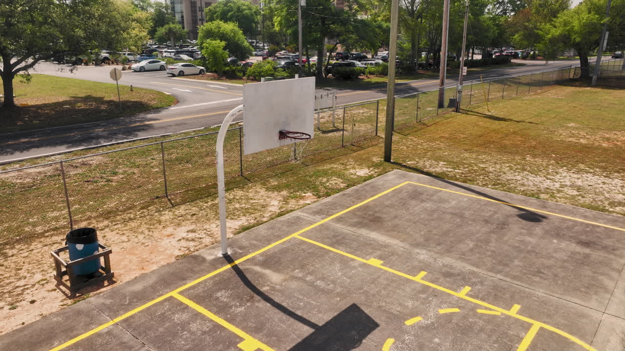 vuelo aéreo hacia adelante sobre una cancha de baloncesto vacía con un coche conduciendo en la carretera en el fondo en el distrito estadounidense