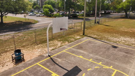 vuelo aéreo hacia adelante sobre una cancha de baloncesto vacía con un coche conduciendo en la carretera en el fondo en el distrito estadounidense