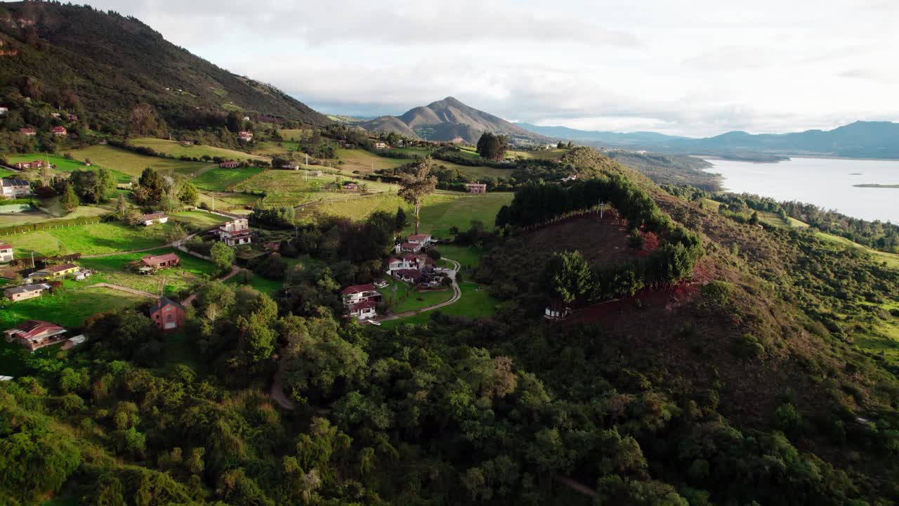 Zoom in shot of countryside houses surrounded by green hills near Guatavita Lake on a sunny morning
