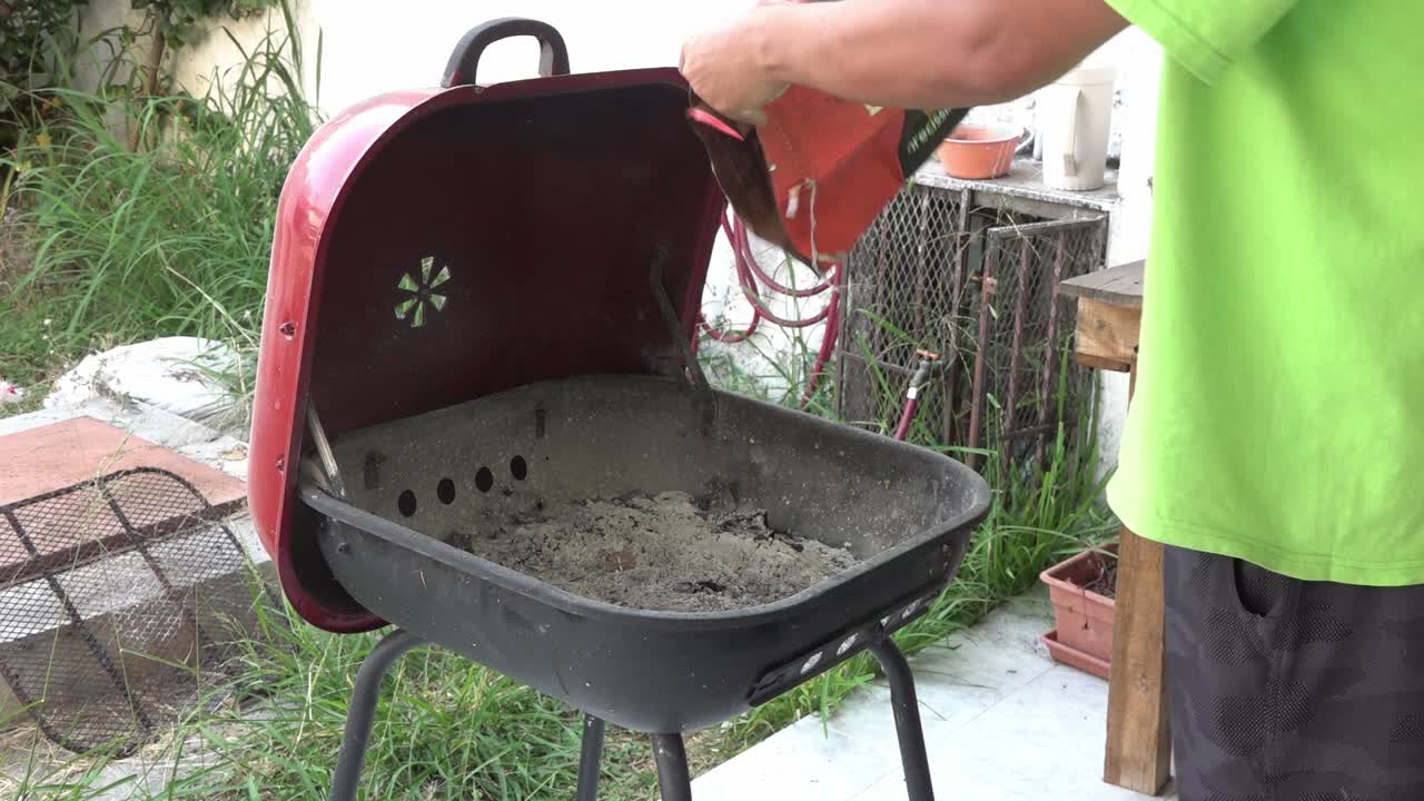 A man pouring charcoal briquettes in a grill