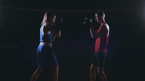 Beautiful-brunette-boxer-working-out-blows-to-the-paws-with-a-trainer-in-a-dark-room