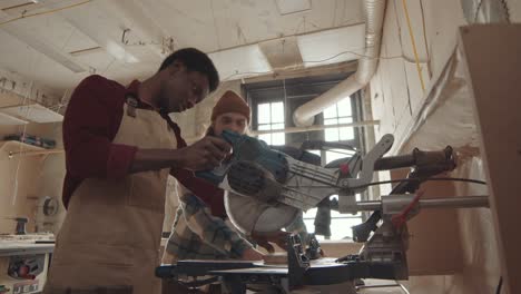 professional joiner watching african-american man using circular saw