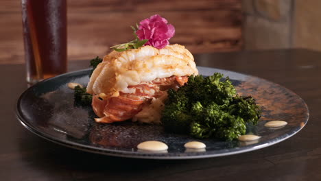 broiled maine lobster tail garnished with roasted broccolini and orzo on a black stoneware plate, slider hd