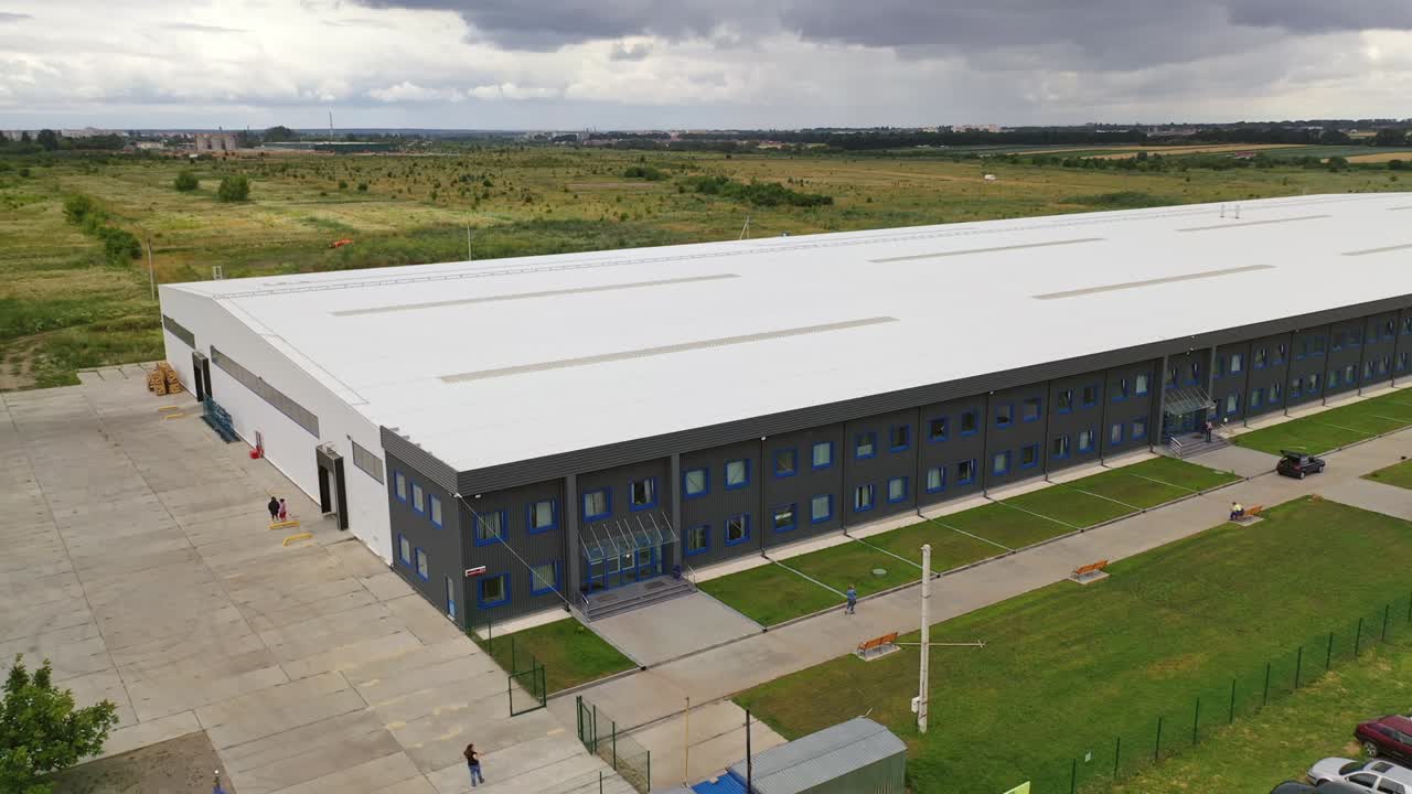 Modern industrial exterior. Large factory building among green fields. New building from outdoors. Aerial view.