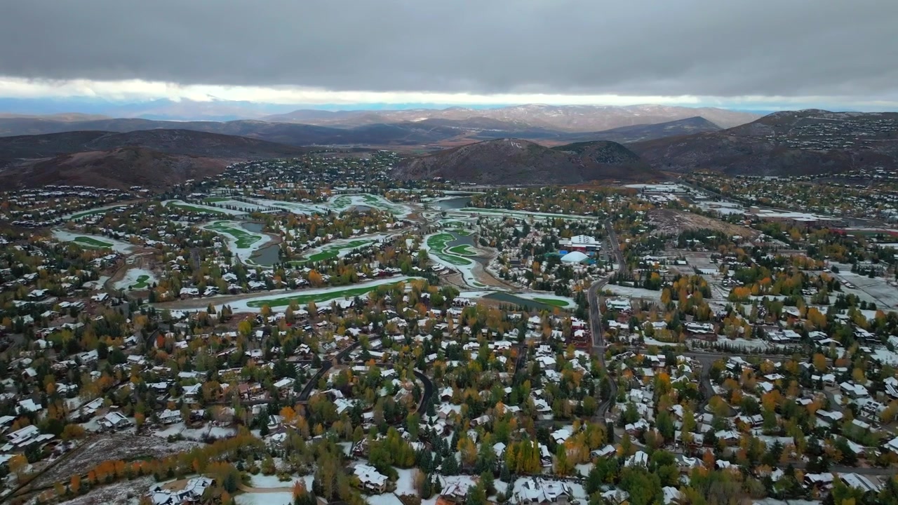 Ripresa aerea con drone del centro di Park City Canyons Village, stazione sciistica olimpica di Vail nello Utah. Un centro di eccellenza per sci e snowboard, in un paesaggio autunnale-invernale con la prima neve e vivaci colori autunnali. Cielo nuvoloso, nevicata, atmosfera nebbiosa e grigia, con case in primo piano.