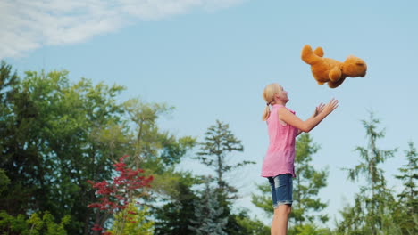 middle aged woman having fun like a child - jumping on a trampoline and throwing up a teddy bear act