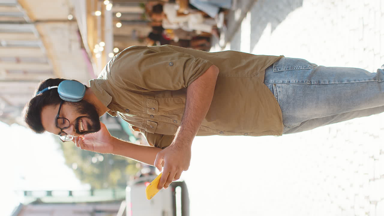 Happy young man in wireless headphones choosing listening music in smartphone dancing outdoors