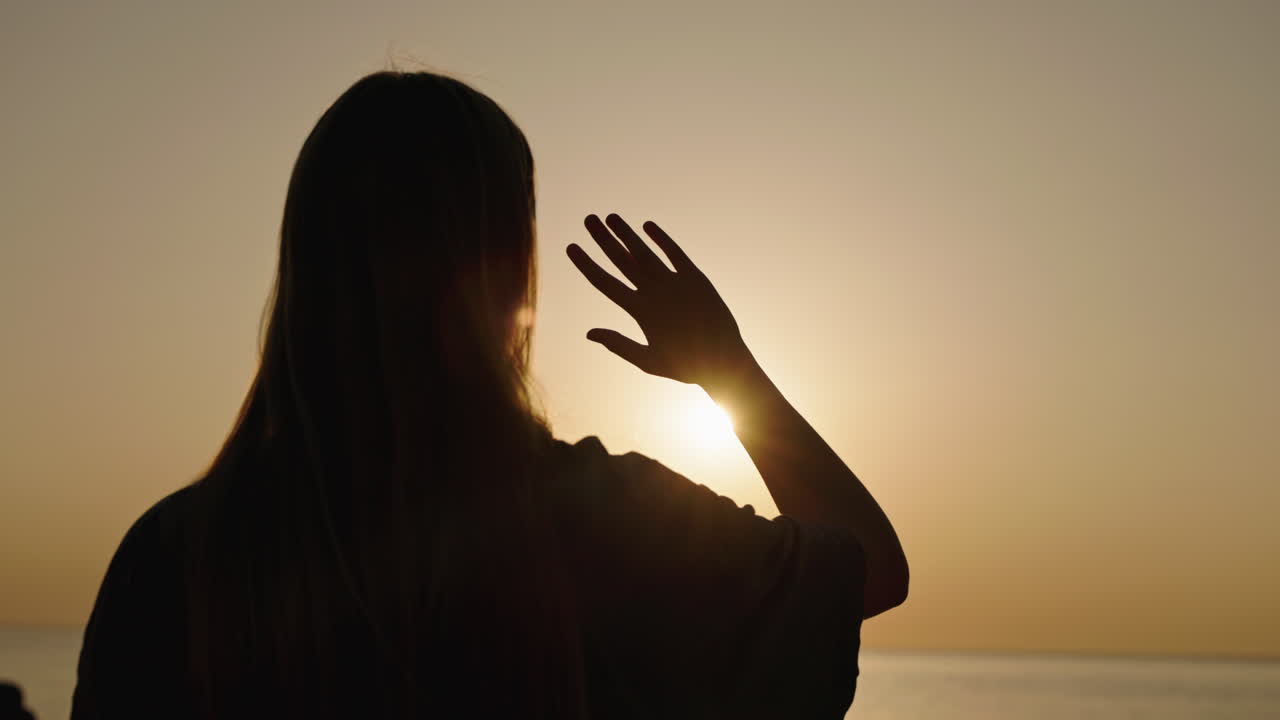 Woman Silhouetted Against Sunset Waving at Ocean