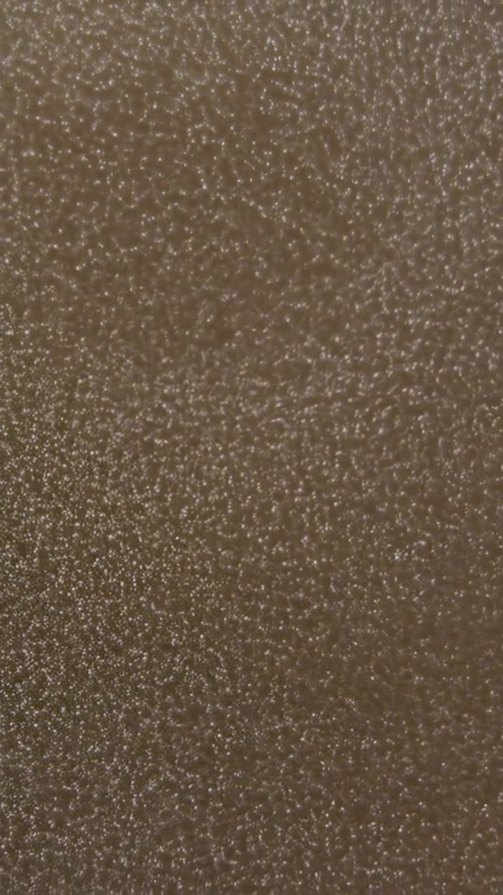 Vertical video: Filming camera capturing closeup brown textured surface in tight frame, with specks