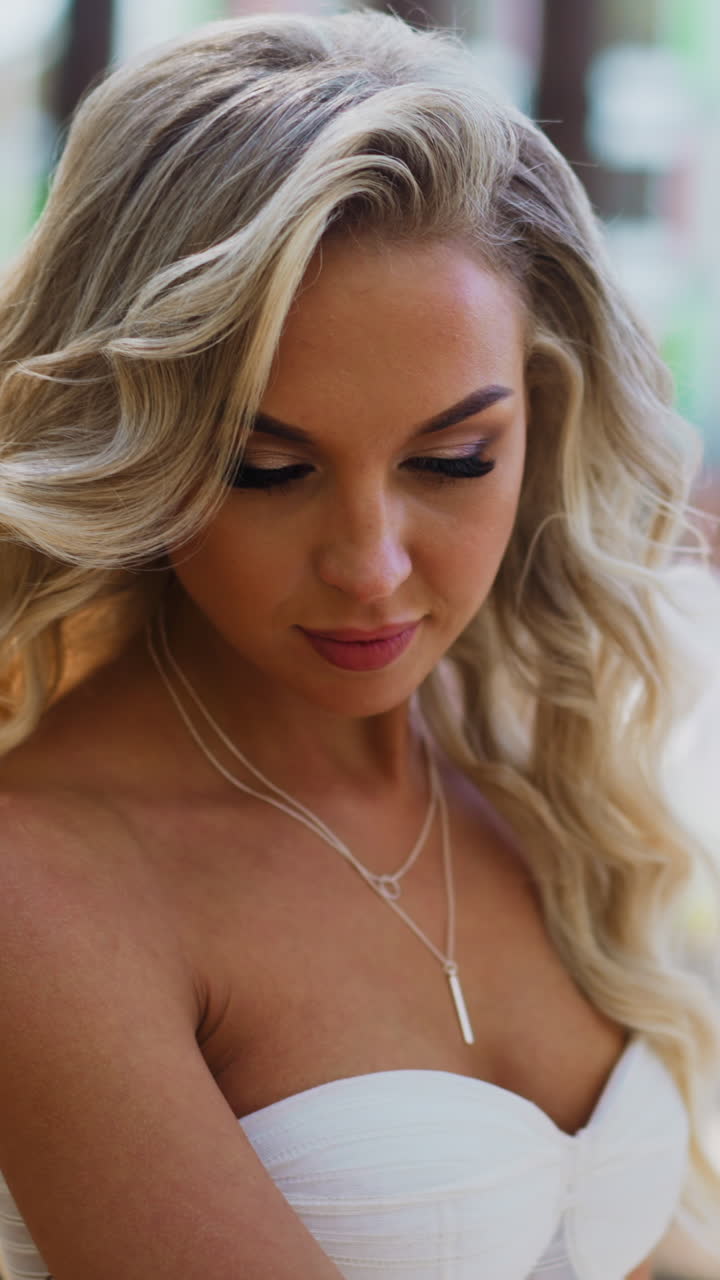Attractive lady bride with long curly hair in white wedding dress waves skirt train standing in green sunny city park close view slow motion