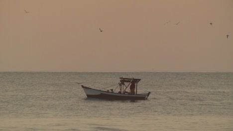 pescador pescando en bote pequeño en el mar, fondo de cielo dorado, atardecer
