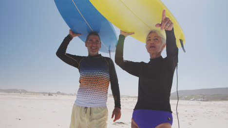 senior caucasian couple holding surfboards above their heads on the beach