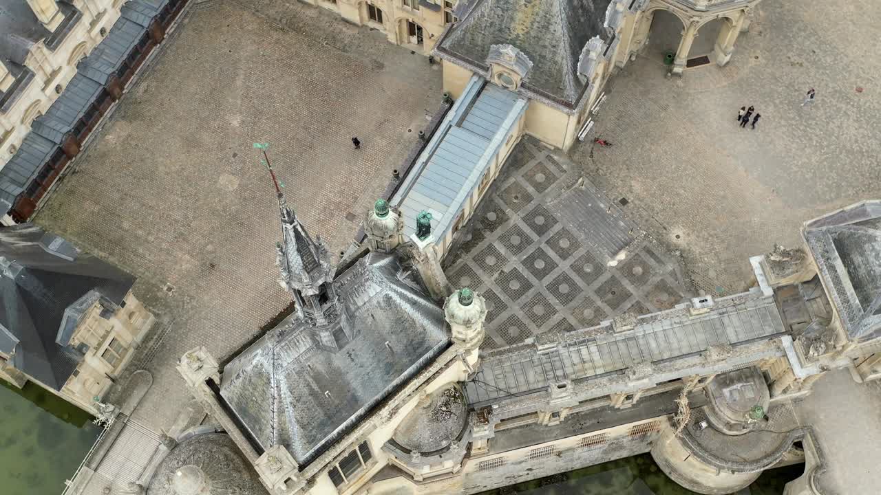 Aerial circling view of Chateau de Chantilly castle courtyard and ornate rooftops, France. Historic French castle architecture, travel, heritage