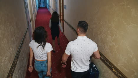 young couple with suitcases in the hallway at hotel. rear view of a man and woman follow the receptionist to their room in the hotel. slow motion.