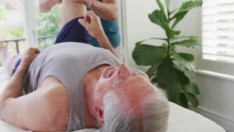 caucasian senior man lying on examining table while being treated by male therapist at health club