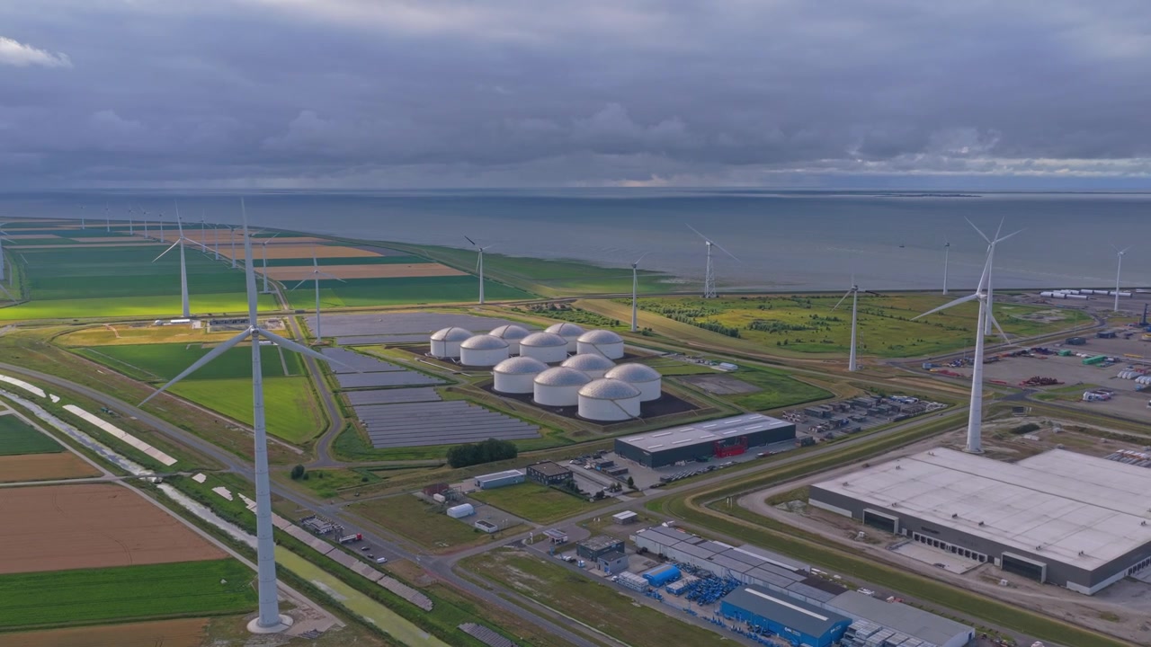 Industrial landscape with large oil storage tanks and a wind farm generating renewable energy. Concept of coexistence between fossil fuels and clean power