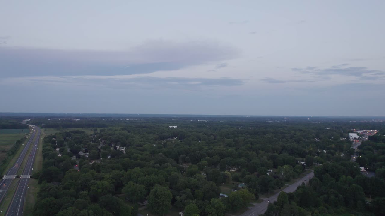 un dron aéreo se disparó hacia adelante sobre las casas de la ciudad rodeadas de árboles verdes al lado de la carretera después de la puesta del sol