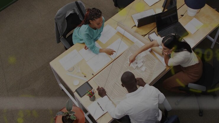 Woman in teal top pointing at blueprint and leading team into arranging cards for office design